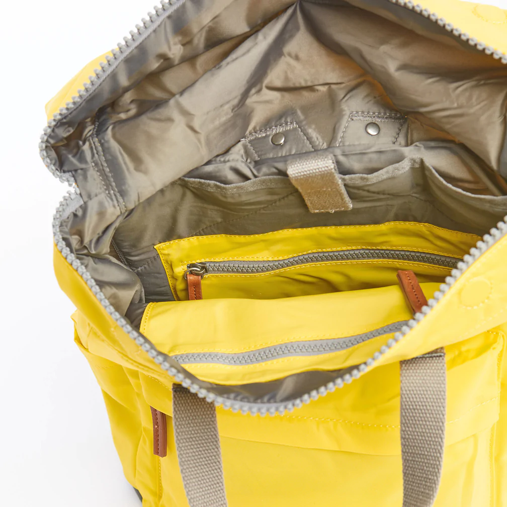 Mochila Roka de nylon reciclado con compartimento delantero y cremallera cubierta en color amarillo. Resistente a la intemperie, duradero, elegante y está hecha de nylon reciclado que le da a la mochila un aspecto suave y muy moderno