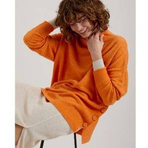 Mi&Co Dalia en color naranja. Jersey oversize de cuello subido y manga larga. Detalle de botones en el lateral. Canalé en puños y bajos. 
